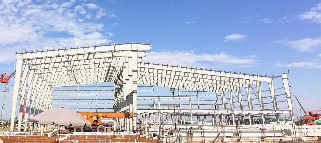 Steel workshop frame erection in progress at a construction site with crane and H-beam columns under blue sky