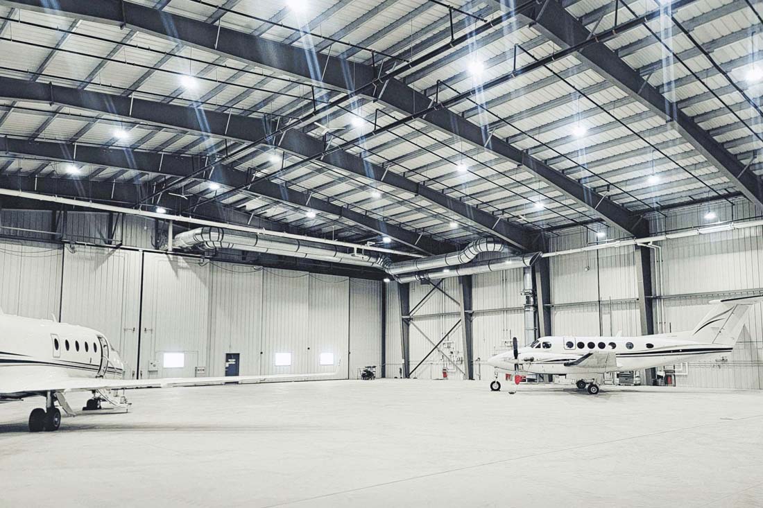 Interior view of a spacious clear-span steel aircraft hangar with private airplanes parked inside