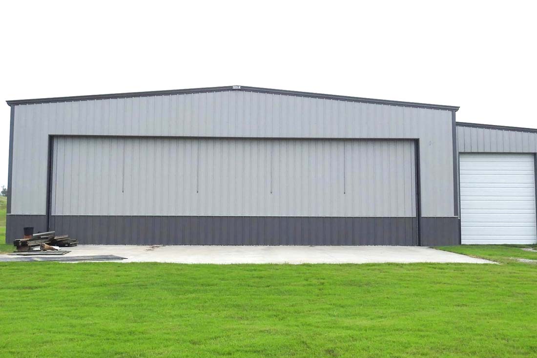 Exterior view of a private steel aircraft hangar featuring a large sliding hangar door