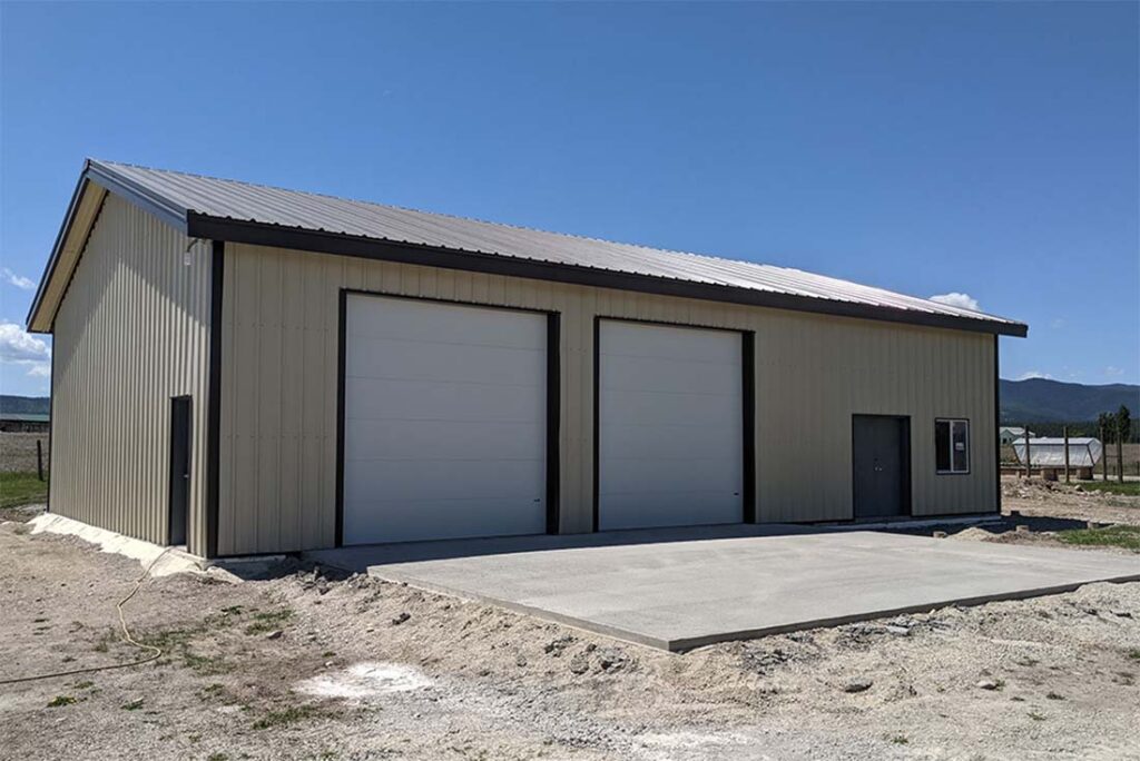 Large metal shed building with steel frame, gable roof, and two roll-up doors, designed for farm equipment, vehicle, and utility storage.