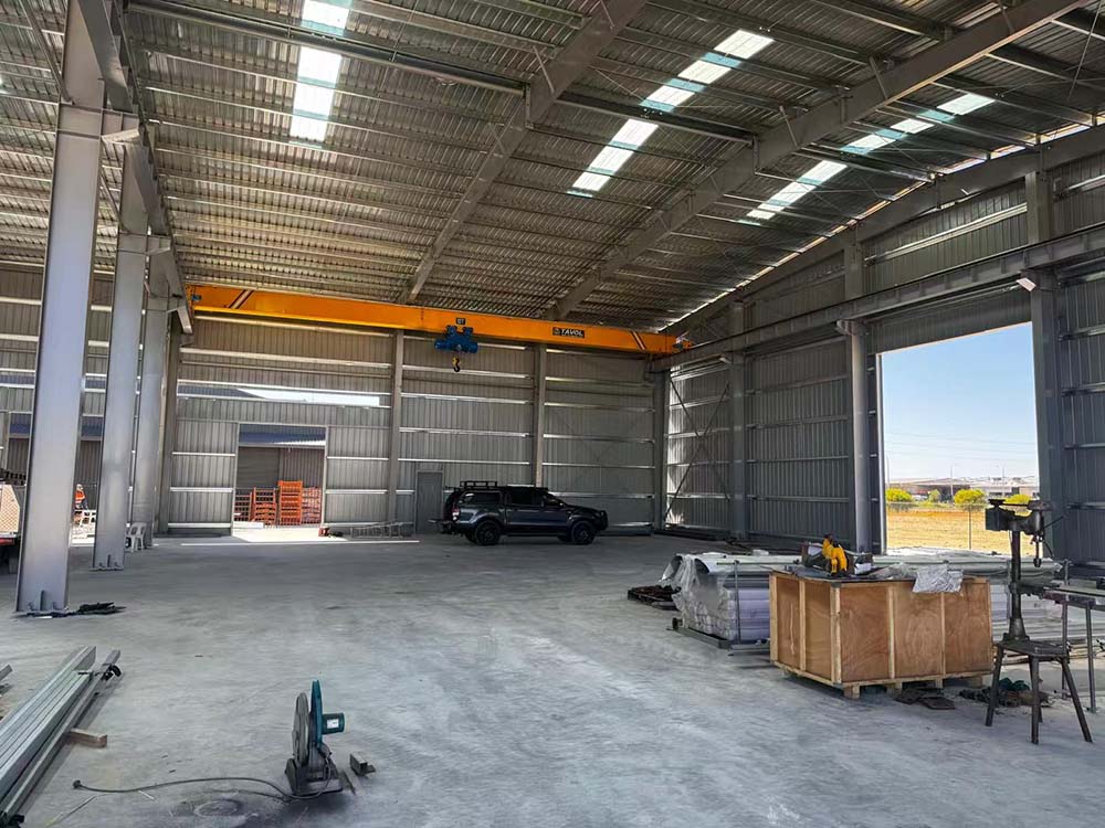 Exterior view of the 25m x 50m x 8m steel workshop under construction with the main steel frame and site access area.