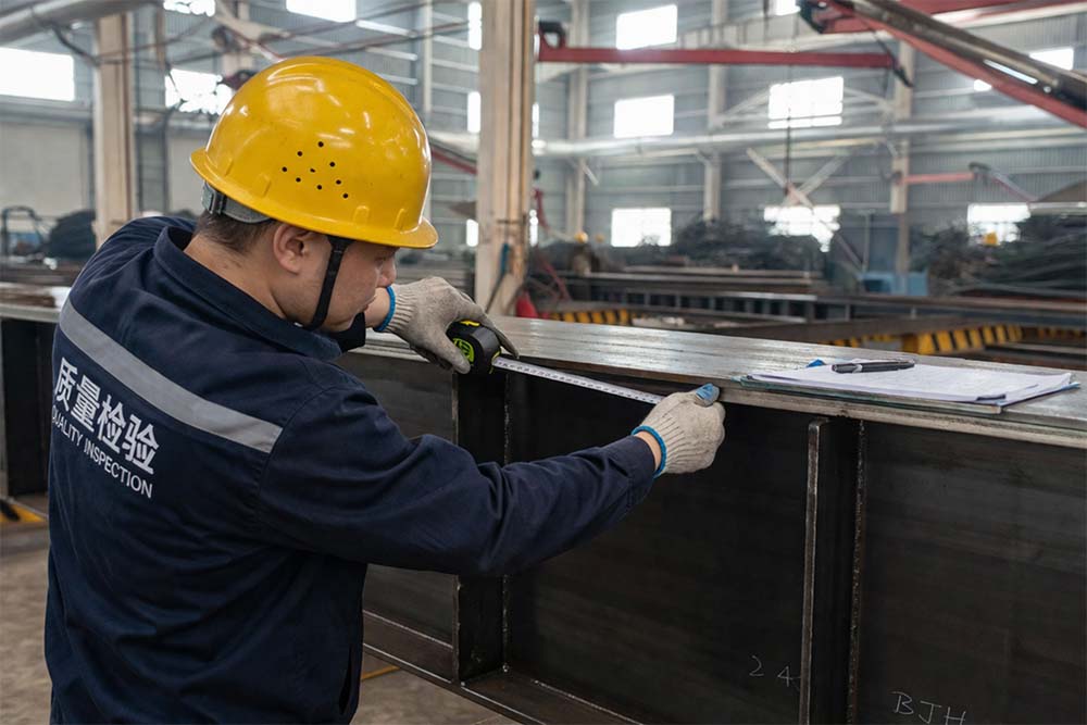 Worker measuring steel member dimensions during fit-up check